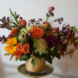 Mixed bouquet of orange, purple, white, and yellow flowers in a gold vase