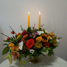 Mixed floral centerpiece with two lit yellow candles in a gold pedestal vase