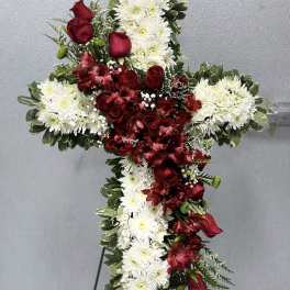 Standing floral cross of white mums and red roses displayed on a metal easel.
