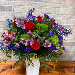 Mixed bouquet of red roses, purple flowers, and green accents in a white vase