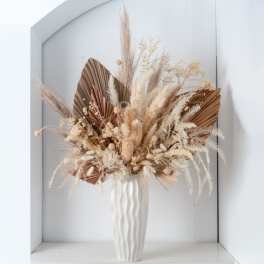 Tall neutral-toned dried floral arrangement with palm leaves and pampas in a white textured vase