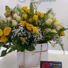 Yellow and white rose bouquet in a white gift bag with a butterfly pick