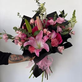 Pink lily and rose bouquet wrapped in black paper with a pink ribbon