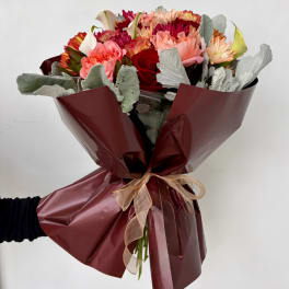 Hand-tied bouquet of mixed roses, carnations, and calla lilies wrapped in burgundy paper