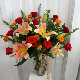 Bouquet of red roses and peach lilies in a glass vase