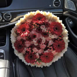 Bouquet of red gerbera daisies and roses wrapped in cream paper