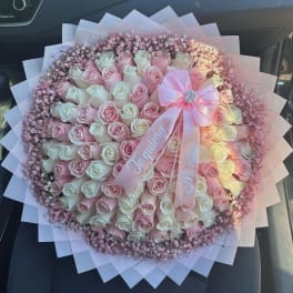 Round bouquet of pink and white roses with a pink ribbon and baby's breath
