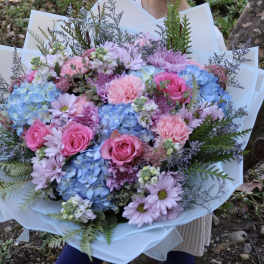 Handheld bouquet of pink roses, blue hydrangeas, and lavender daisies