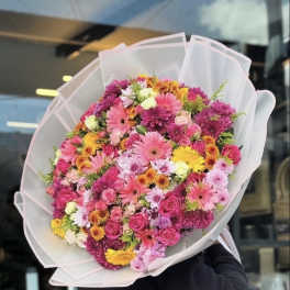 Large mixed bouquet of pink, yellow, and orange flowers wrapped in white paper
