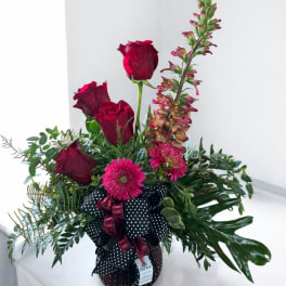 Red roses and pink flowers in a black polka-dot vase with ribbon