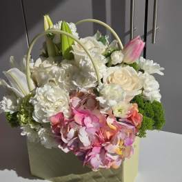 Mixed flower arrangement in a pale green gift bag with pink and white blooms