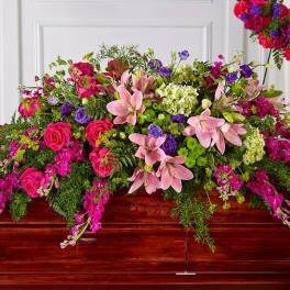 Large pink and purple floral casket spray on a wooden casket