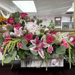 Pink roses and lilies arranged in a floral basket with a teapot centerpiece