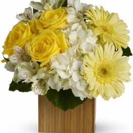 Yellow roses and pale yellow daisies in a wooden cube vase