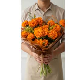 Person holding a bouquet of orange marigolds wrapped in brown paper