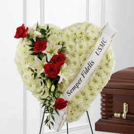 Heart-shaped funeral wreath with red roses and white lilies beside a casket