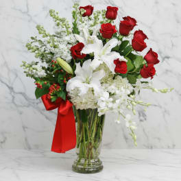 Red roses and white lilies in a clear glass vase with a red ribbon