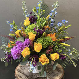 Bright mixed bouquet with yellow roses, purple carnations, and blue delphinium in a vase