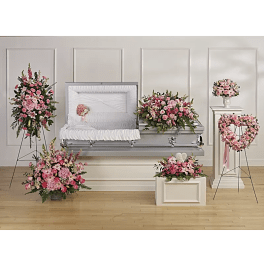 Pink floral funeral casket spray with matching arrangements around a white casket
