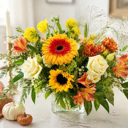 Colorful autumn bouquet in a clear glass vase with sunflowers, roses, and gerberas