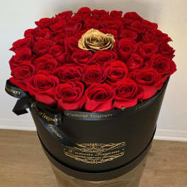 Red roses in a black round box with a gold rose at center