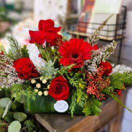 Red roses and a red gerbera daisy in a glass vase with berries and greenery