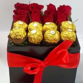 Red roses and gold-wrapped chocolates in a black gift box with a red ribbon