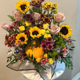 Autumn floral arrangement with sunflowers, roses, and chrysanthemums around a pumpkin