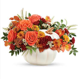 Orange and red floral arrangement in a white pumpkin vase