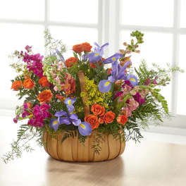 Colorful flower arrangement in a wooden basket with orange roses and purple irises