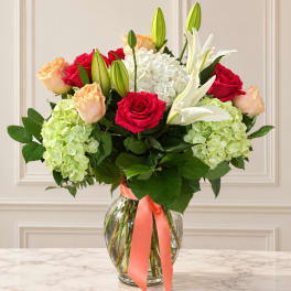 Bouquet of red and peach roses with white lilies and hydrangeas in a glass vase