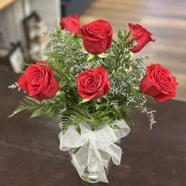 Red roses arranged in a clear glass vase with a white ribbon