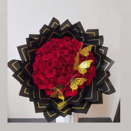 Large bouquet of red roses wrapped in black paper with gold trim and butterfly accents