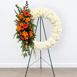 Standing floral wreath with white blooms and an orange mixed spray on the left