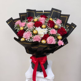 Bouquet of pink and red roses with white filler flowers and gold chocolates
