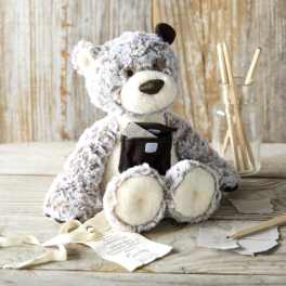 Plush teddy bear holding a small gift box beside a glass jar with sticks
