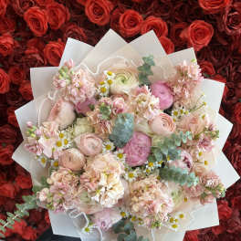 Pink bouquet with roses, ranunculus, and small daisies in white wrap