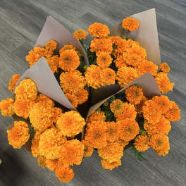Bundles of orange marigolds wrapped in brown paper on a gray floor