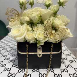 Cream roses arranged in a black handbag-style box with gold butterfly accents