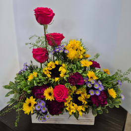 Mixed floral arrangement with pink roses, yellow sunflowers, and purple daisies in a wooden box