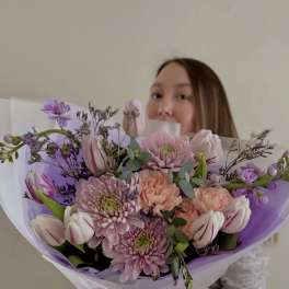Woman holding a pastel bouquet of tulips and chrysanthemums wrapped in lavender paper