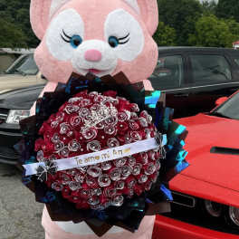 Pink bunny mascot holding a red rose bouquet with a ribbon
