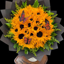 Bouquet of orange sunflowers with butterfly decorations in black wrap