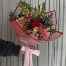 Handheld bouquet of pink and red flowers wrapped in pink paper with a ribbon