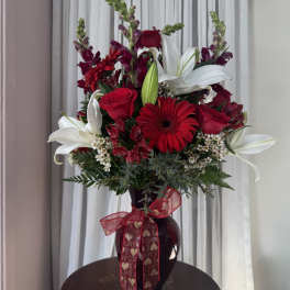Red and white floral arrangement in a dark vase with a heart ribbon