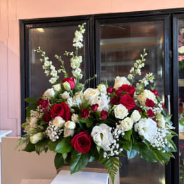 Large arrangement of red and white roses with tall white blooms in a wooden container.