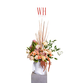 Tall floral arrangement in a white bag-style container with pink and cream blooms