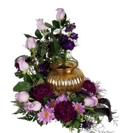 Lavender and deep purple floral cremation arrangement surrounding a gold glass urn