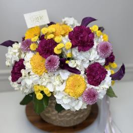 Mixed bouquet of white, yellow, magenta, and lavender flowers in a basket