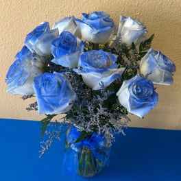 Blue-tinted white roses in a glass vase with a blue ribbon